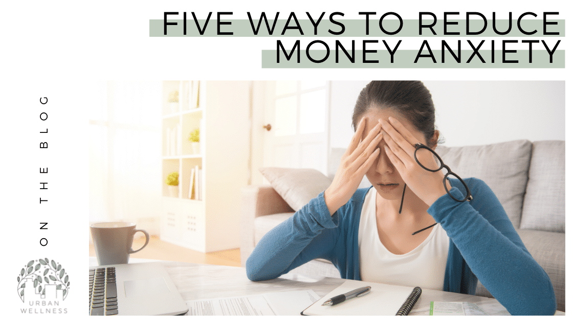 A graphic that reads "On the blog: 5 Ways to Reduce Money Anxiety" above a stock photo of a dark haired white woman sitting at a table with her face in her hands, like she is stressed.
