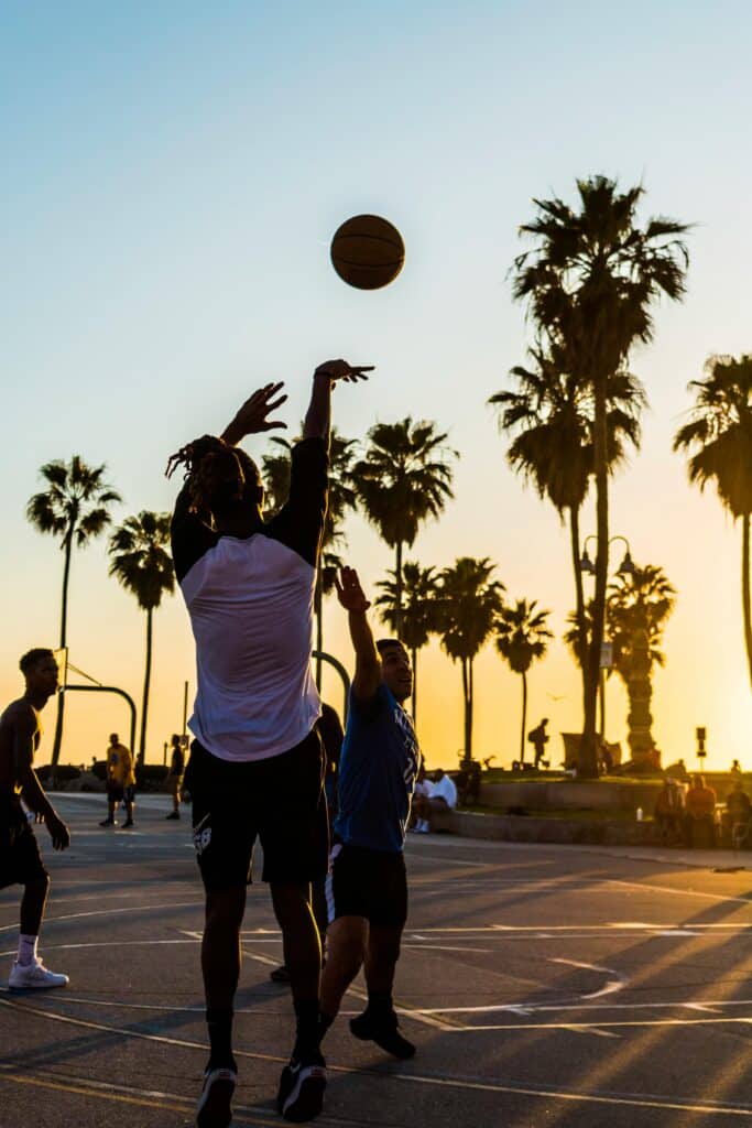 a person in shadow shoots a basketball, with teammates running in the background