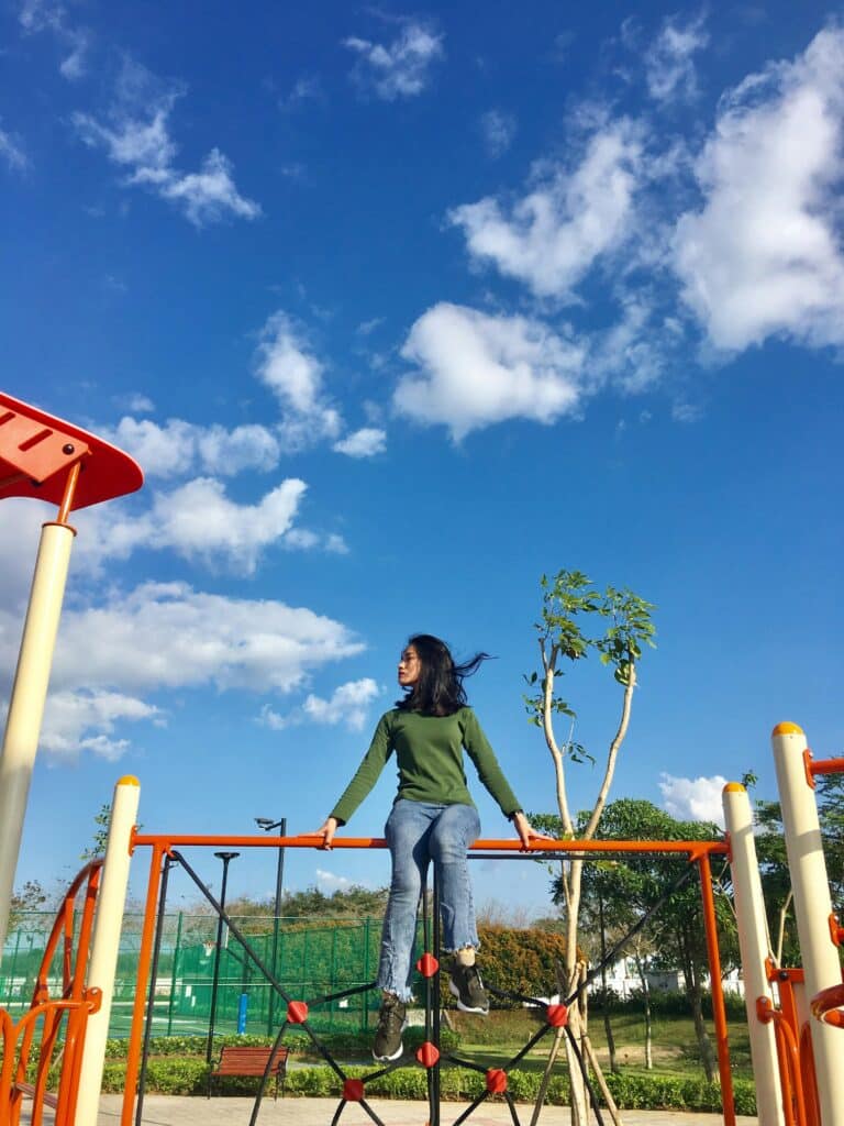 a woman sits on top of a children's jungle gym on a sunny day