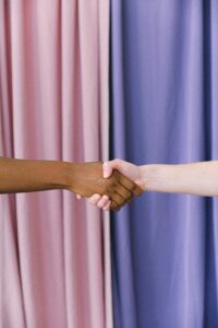 a Black arm and a white arm clasp hands in front of a multi-colored curtain